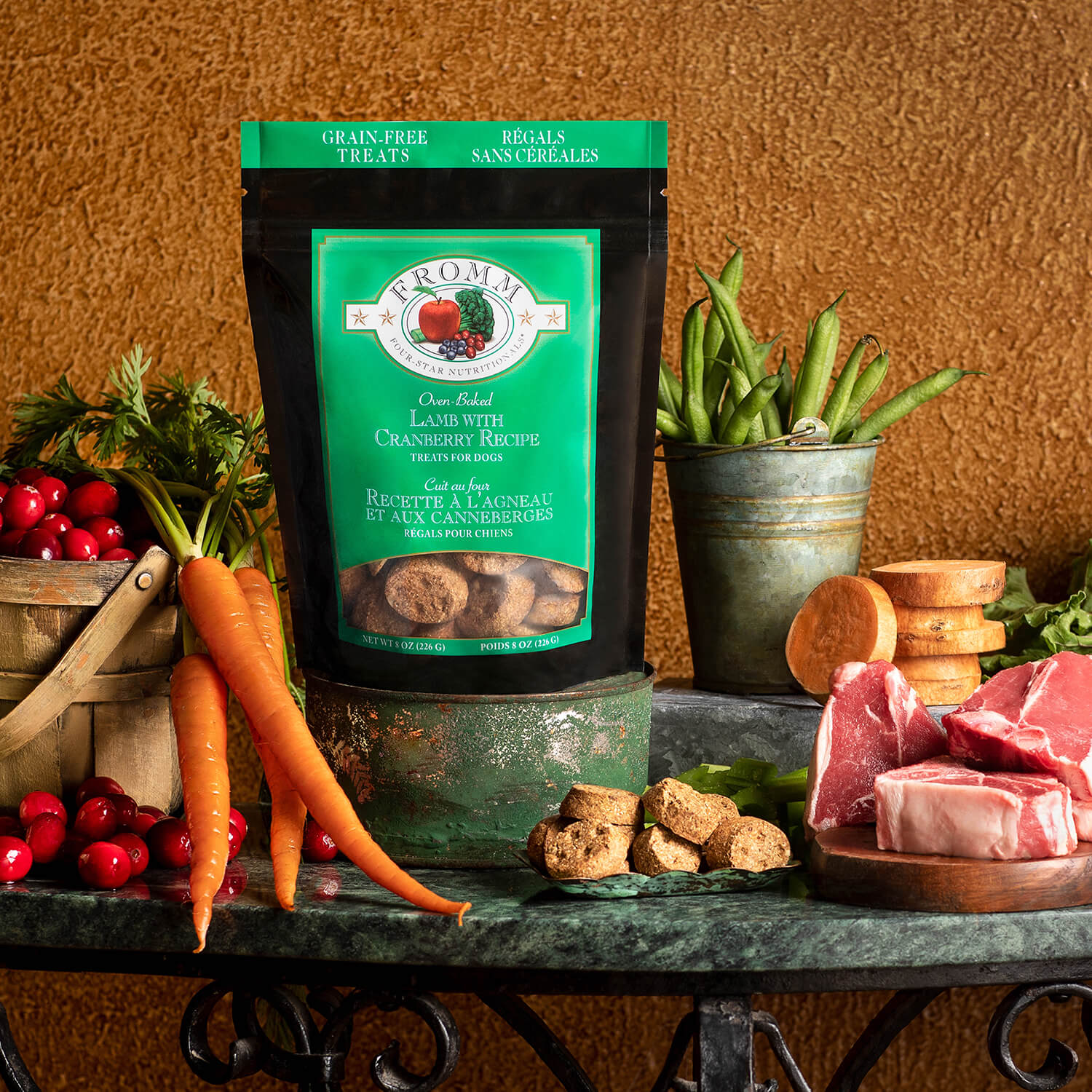 Bag of Fromm dog treats on a table with carrots, cranberries, and other ingredients.